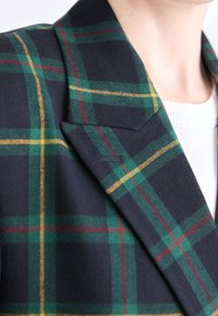 Veston en mélange de laine avec une base bleu marine foncé et un motif à carreaux vert, jaune et rouge, col cranté et tissu texturé.