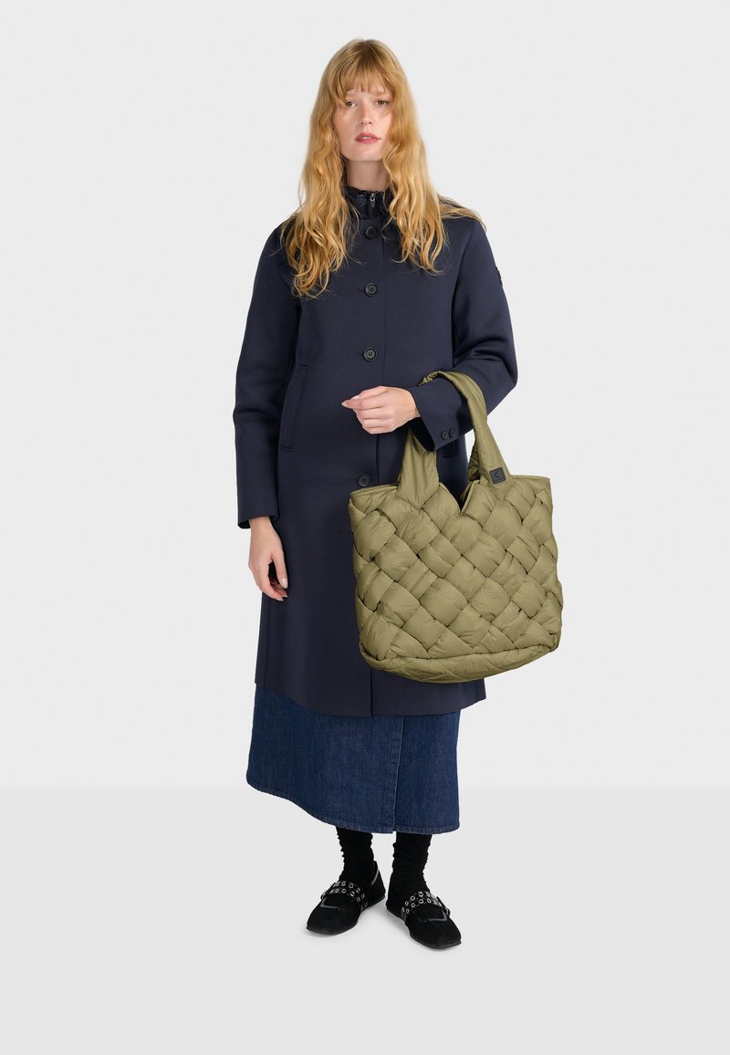Cappotto blu navy con grandi bottoni, abbinato a una borsa a tracolla verde oliva puffosa con motivo trapuntato e due manici solidi. Gonna di jeans e calzature nere.