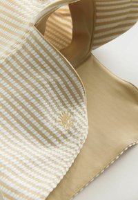 Csíkos anyag bézs és krémszínekben, sima tapintású és hímzett logóval. Egyszínű, puha bézs alsó oldal.
