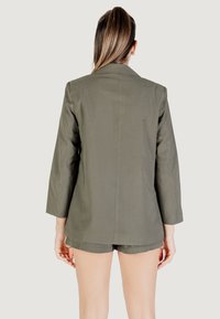 Blazer verde oliva con maniche lunghe, dal taglio sartoriale e texture liscia. Presenta una cucitura posteriore e un design delle spalle leggermente oversize.