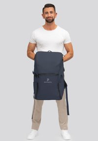 Zaino blu navy con logo, scomparti con zip, spallacci regolabili e una trama di tessuto liscia e resistente. Design leggero.