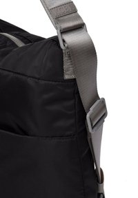 Bolsa negra con una superficie lisa y texturizada, que cuenta con una correa de hombro gris y un hebilla ajustable. Detalle del bolsillo lateral visible.