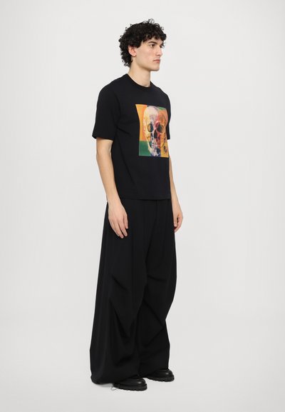 Black cotton t-shirt featuring a colorful skull graphic, paired with loose black trousers. Overall minimalist and modern design.