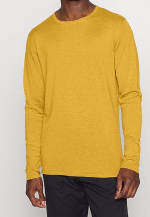 Gelbes langärmliges T-Shirt aus weichem Stoff mit Rundhalsausschnitt, das in einem lockeren Schnitt und mit minimalen Nähten entworfen wurde, getragen mit schwarzen Hosen.