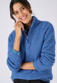 Maglione realizzato in tessuto lavorato a maglia color azzurro chiaro con collo alto, mezza cerniera e motivo a trecce. Presenta polsini e orlo a costine.