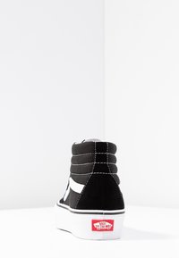 Scarpa alta Vans in bianco e nero con cuciture visibili e logo rosso "Vans Off The Wall" sulla suola bianca, vista da dietro.