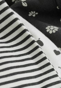 Schwarz-weißer Stoff mit horizontalen Streifen und einem floralen Muster. Glatte Textur mit kontrastierenden Designs und Farben.