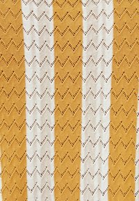 Textiel met afwisselende verticale strepen in mosterdgeel en wit, met een zigzagpatroon en open brei-details door het geheel.