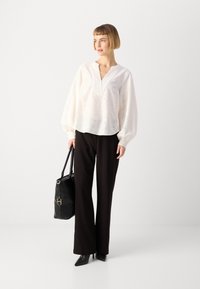 Blusa bianca ricamata con scollo a V e maniche a palloncino abbinata a pantaloni neri a gamba larga e borsa nera, con tacchi a punta.
