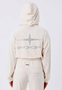 Sudadera color crema con capucha y puños acanalados. Presenta un logotipo brillante y un diseño de estrellas en la parte posterior. Tejido suave con un ajuste holgado.