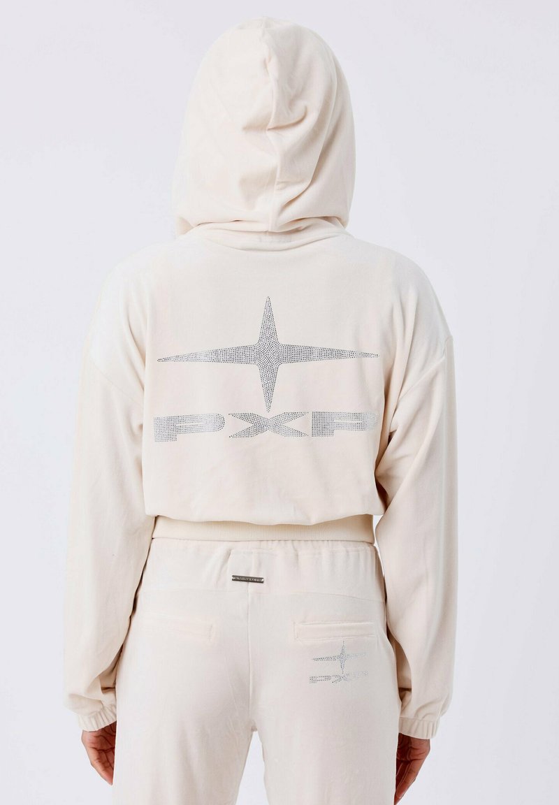 Sudadera color crema con capucha y puños acanalados. Presenta un logotipo brillante y un diseño de estrellas en la parte posterior. Tejido suave con un ajuste holgado.