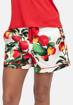 Osoba nosząca białe szorty z nadrukiem czerwonych i żółtych owoców oraz zielonych liści, połączone z częściowo widoczną czerwoną koszulą.