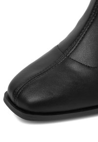 Čierna kožená čižma s špicatou špičkou a minimálnym štepením. Má hladký povrch a plochú gumovú podrážku pre stabilitu.
