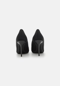 Črne visoke pete z izostrenim nosom in gladkim zgornjim delom iz blaga. Ponašajo se z elegantno stiletto peto in minimalnimi šivi.
