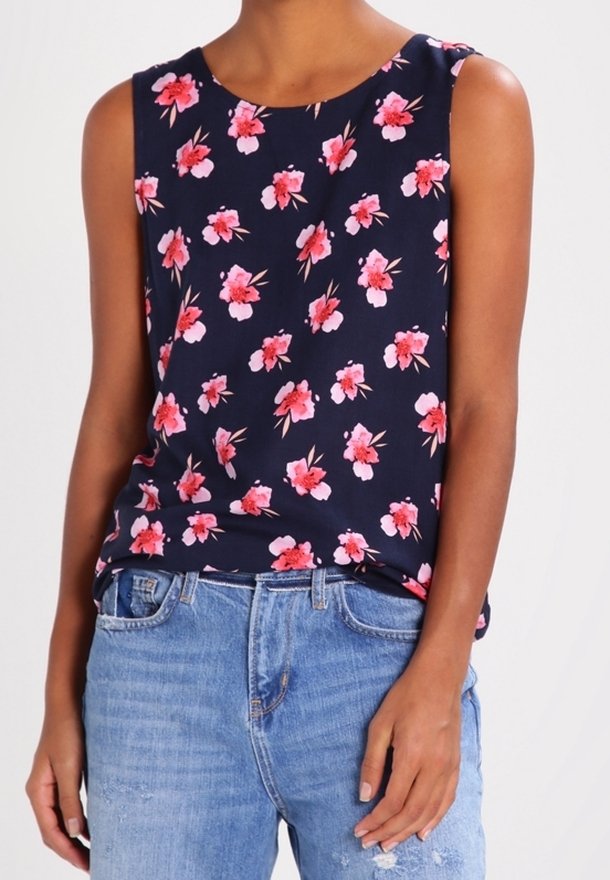 Marinebluse ohne Ärmel mit floralen Mustern in Pink und Weiß sowie grünen Blättern; glattes Material mit Rundhalsausschnitt, kombiniert mit hellblauen Jeans.
