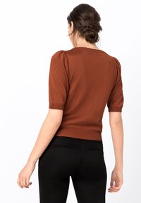 Bronze short-sleeve sweater with puffed shoulders, ribbed neckline, and hem. Paired with high-waisted black pants. Soft knit texture.