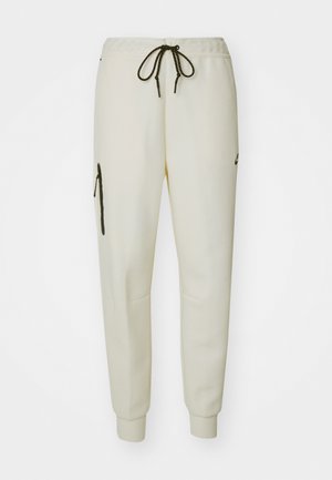 Pantalons de jogging couleur crème avec taille élastique, cordon de serrage ajustable, poches latérales et poche zippée sur la cuisse gauche.