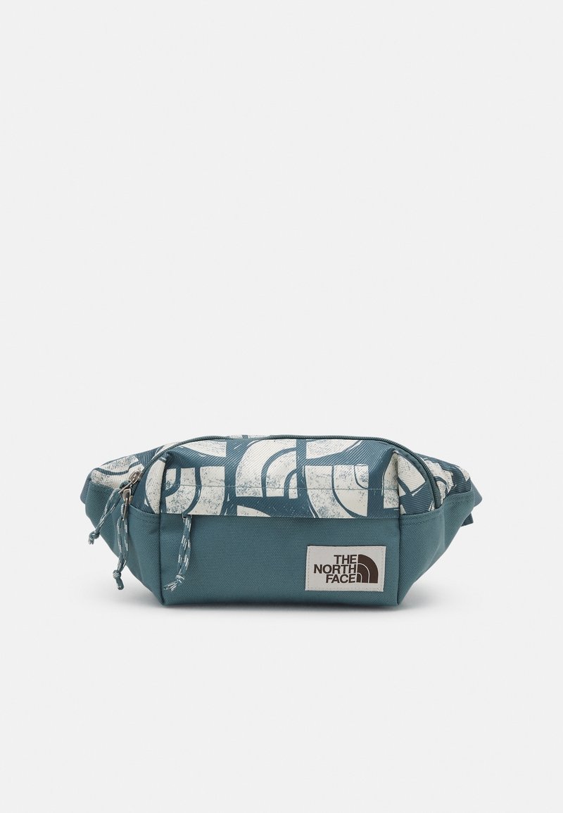 Petit sac banane bleu sarcelle et blanc avec motif abstrait, compartiments zippés et un patch rectangulaire portant le logo The North Face à l'avant.