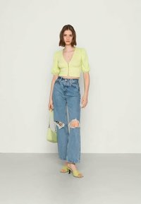 Top cropped verde-lima com mangas curtas bufantes, combinado com jeans desfiados de cintura alta em azul claro, sandálias de salto verdes e mala a condizer.