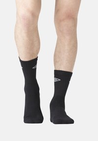 Chaussettes noires de cheville avec une texture côtelée, présentant des accents de motif en losange blanc sur les côtés, offrant un ajustement confortable autour des chevilles.