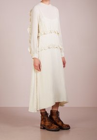 Bílé šaty s černými puntíky, volánkovými rukávy a rozšířenou siluetou. Hnědé kostkované šněrovací boty s robustní podrážkou.