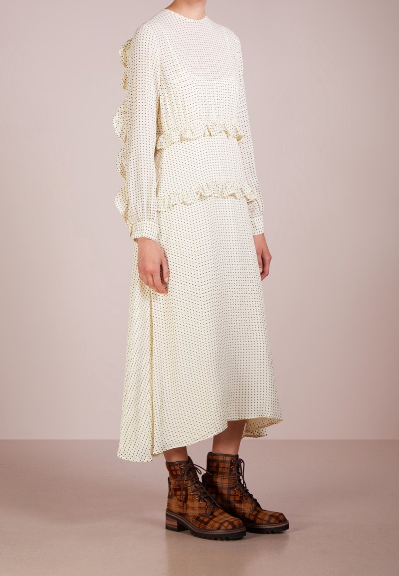 Bílé šaty s černými puntíky, volánkovými rukávy a rozšířenou siluetou. Hnědé kostkované šněrovací boty s robustní podrážkou.