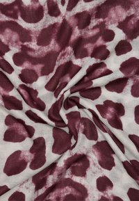 Tkanina o beżowym tle z dużymi czerwonawo-burgundowymi abstrakcyjnymi plamami, o gładkiej strukturze i subtelnym połysku.