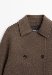 Dubbelknäppt brunt yllekappa med slagkrage och svarta knappar, med en mjuk textur och rena sömnadsdetaljer.