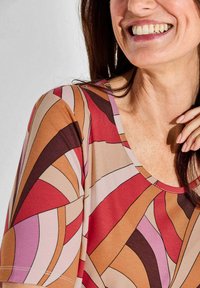 Bunt gemustertes Oberteil mit rundem Ausschnitt und kurzen Ärmeln, mit abstrakten Mustern in Rot-, Pink-, Beige- und Brauntönen. Weiche Textur.