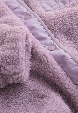 Lilaksi fleece-vaate, jossa on pehmeä ja teksturoitu pinta. Ominaisuuksiin kuuluvat kiiltävä lilaksi kangas ja pyöreät nepparit. Lämmin ja muhkea muotoilu.