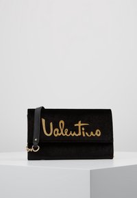 Svart mocka clutch-väska med en vikbar design, guld- logotypdetalj och en avtagbar axelrem. Slät textur med minimal hårdvara.
