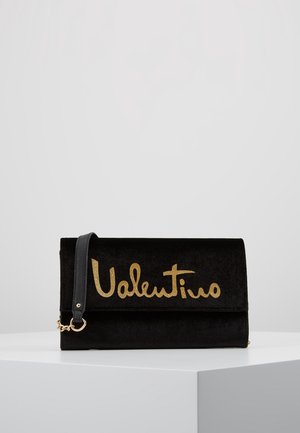 Black suede clutch bag featuring a fold-over design, gold logo accent, and a detachable shoulder strap. Smooth texture with minimal hardware.