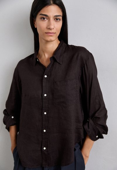 Chemise en lin foncé avec un design à col boutonné, une poche poitrine unique et des manches retroussées. Présente des boutons blancs et une coupe décontractée.