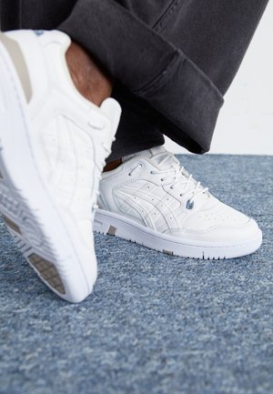 White athletic shoes featuring a smooth leather upper, perforated detailing, and contrasting gray accents. Rubber sole with textured tread.