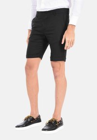 Pantaloni corti neri su misura in tessuto leggero, con una vestibilità slim, orli risvoltati e tasche laterali. Abbinati a scarpe in pelle nere.
