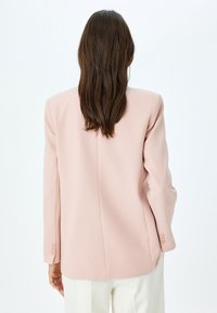 Helles rosa Blazer mit tailliertem Design, strukturierten Schultern und Details mit drei Knöpfen an den Bündchen, aus einem glatten Stoff gefertigt.