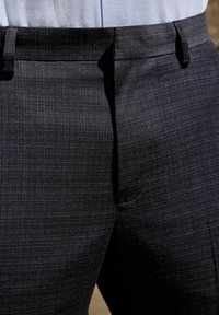 Pantalons gris foncé sur mesure avec un motif texturé subtil. Dispose de passants de ceinture et d'un design à l'avant plat pour une silhouette élégante.