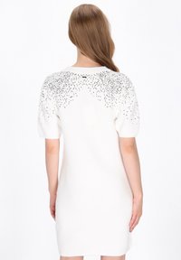 Rochie albă tricotată, cu mâneci scurte tip puff și embellishments argintii pe umeri, subliniind textura și detaliile decorative.
