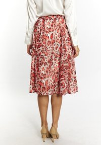 Gonna midi a stampa leopardata rossa e rosa con vita arricciata. Tessuto fluido con una consistenza liscia. Indossata con scarpe col tacco alte beige.
