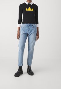 Pull noir en tricot avec un motif de couronne jaune et un col blanc. Jean bleu clair taille haute et bottines noires épaisses complètent le look.