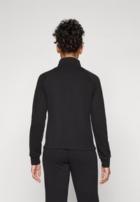 Chaqueta deportiva negra con cuello alto, mangas largas y una textura suave, combinada con pantalones a juego. Diseño simple y minimalista.