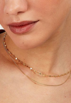 Gold- und silberne geschichtete Halsketten mit runden und ovalen Gliedern, die auf der oberen Kette strukturierte Akzente und auf der unteren eine glatte Oberfläche aufweisen.
