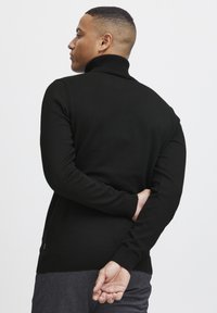 Schwarzer Rollkragenpullover mit geripptem Kragen und Bündchen, glatter Textur, figurbetontem Design und einem kleinen Logo-Detail am Saum.
