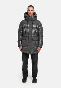 Puffer jacket in shiny dark grey, with a hood, two front pockets, and a zip closure. Features thick insulation and a slightly loose fit.