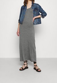 Gray maxi dress made of soft fabric, paired with a denim jacket. The outfit is complemented by black strappy sandals, featuring a flat sole.