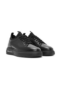 Zapatillas de cuero negro con un acabado suave, punta redondeada, diseño con cordones, cuello acolchado y una unidad de amortiguación de aire visible en la suela.