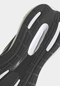 Suela de zapatilla en blanco y negro con goma texturizada, que presenta estrías y un inserto de espuma blanca etiquetado como "CLOUDFOAM" para mayor amortiguación.