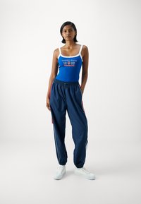 Blå ribbet tanktop med hvite stropper og logo; marineblå joggebukser med røde detaljer og sidestrekker; hvite joggesko.