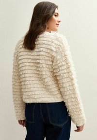 Maglione di un colore crema fuzzy con texture e strati a righe; design cropped con maniche lunghe; abbinato a jeans di denim blu scuro.