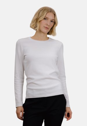 Hvit langermet topp laget av mykt stoff med rund halslinning, med en tettsittende design og jevn tekstur, sammen med mørke bukser.